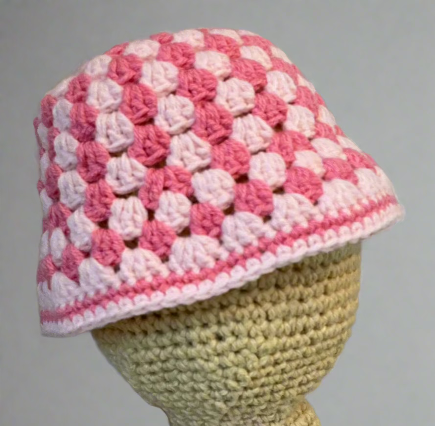 A crochet granny stitch bucket hat with alternating bands of hot pink and baby pink, displayed on a mannequin head.