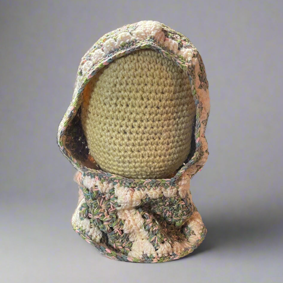 A crochet balaclava hood with a floral pattern made from an acrylic mix, displayed on a mannequin head.